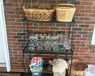 Metal Shelving Unit with Baskets and Glassware - A sturdy metal shelving unit featuring various baskets and a collection of glassware. Ideal for storage or display in any room.