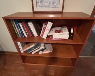 Wooden Bookshelf with Cookbooks and Decor - A wooden bookshelf featuring a collection of cookbooks and a decorative framed picture. Ideal for organizing books or displaying items.