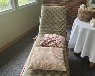 Vintage Chaise Lounge with Cushions - A vintage chaise lounge featuring a green and tan patterned cushion, accompanied by two decorative pillows. Perfect for relaxing in a sunroom or patio.