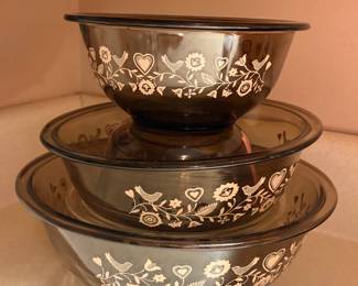 vintage Pyrex mixing bowls in the "Festive Harvest" pattern, featuring a white folk art design of birds, hearts, and flowers on smoky amber glass