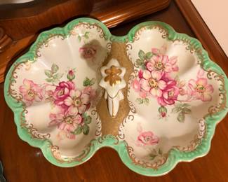 antique divided porcelain dish is a hand-painted piece from the Nippon Era (1891–1921). It features a classic Art Nouveau design with vibrant pink roses, a soft green border, and ornate gold gilding