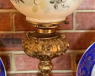 Bradley & Hubbard banquet lamp features a brass base with ornate detailing and a hand-painted glass globe