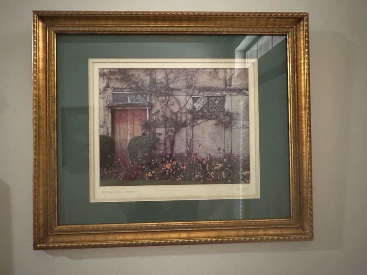 Framed Landscape Wall Art Print ā This framed landscape wall art print features a serene outdoor scene with muted natural tones and floral details. It is enclosed in a decorative gold frame with ornate detailing and a green mat border, enhancing its classic appeal. Measuring approximately 26 inches wide by 22 inches tall, this print is well-suited for accenting living room or hallway walls. The frame and print are in good condition with no visible damage or discoloration. An elegant piece that adds subtle charm to any home decor.