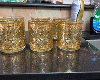 Vintage 1960s Culver 'Valencia' 22K Gold — This vintage set of six rocks glasses features a raised intricate gold and green design that adds a touch of elegance to any kitchen or bar. Each glass is clear with ornate, detailed metallic accents that showcase quality craftsmanship and vintage style. They measure approximately 3.5 inches in height and 3 inches in diameter, perfect for serving cocktails or spirits. The glasses are in good condition with minimal wear to the gilded decoration and no chips or cracks. These distinctive glasses make a charming addition to both casual and formal gatherings.