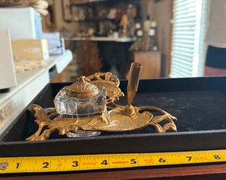 Brass Fountain Pen Ink Well Holder — Gorgeous vintage brass fountain pen ink well holder with original glass ink well and chained lid as noted by the seller. Ornate cast brass base with decorative openwork, fitted pen rest, and a square glass inkwell with a matching hinged lid on a short chain. Overall compact desk accessory measuring approximately 8.5 inches long by 5 inches wide and about 2.5 inches tall, perfect for a writing desk or display. In good vintage condition with expected surface wear and patina to the brass; glass inkwell intact with no visible chips.