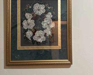 Gregory Frazier Floral Wreath Needlepoin — This Gregory Frazier floral wreath needlepoint artwork captures a beautiful arrangement of white magnolias surrounded by foliage and small fruits. The piece is housed in an ornate gold-tone frame with a double mat in dark green and gold, enhancing its classic appeal. Measuring approximately 29 inches high by 26 inches wide, this framed needlepoint is a striking addition to any traditional decor setting. The condition is good with no visible damage to the needlework, frame, or glass. This piece bears the artist's signature, adding to its collectible value.