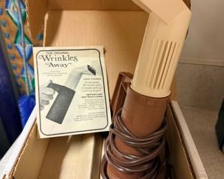 Wrinkles Away Electric Hand Steamer — Wrinkles Away electric hand steamer in original box — a compact travel and home-use garment steamer from Franzus Company. Brown plastic body with angled steam head and included instruction leaflet; designed to steam away wrinkles from wearing apparel without an ironing board. Compact size makes it convenient for closets, luggage, or a laundry room touch-up tool; cord stored around the base in photos. In fair condition cosmetically with original box showing age and light wear; functionality not tested so being sold as-is.