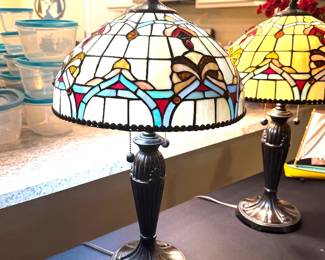 Enhance your home with this elegant pair of Tiffany-style art glass table lamps, beautifully crafted with richly colored stained glass shades featuring warm amber, ivory, ruby, and soft blue accents. The classic bronze-finished bases and dual pull-chain switches offer both timeless beauty and everyday functionality. Whether placed on matching end tables, in a formal living room, den, or primary bedroom, these lamps create a warm, inviting ambiance and serve as stunning statement pieces. Their timeless design complements traditional, Craftsman, Mission, and upscale transitional interiors. A beautiful addition to any Villages home where quality furnishings and classic design are appreciated.