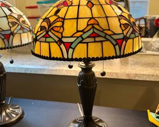 Enhance your home with this elegant pair of Tiffany-style art glass table lamps, beautifully crafted with richly colored stained glass shades featuring warm amber, ivory, ruby, and soft blue accents. The classic bronze-finished bases and dual pull-chain switches offer both timeless beauty and everyday functionality. Whether placed on matching end tables, in a formal living room, den, or primary bedroom, these lamps create a warm, inviting ambiance and serve as stunning statement pieces. Their timeless design complements traditional, Craftsman, Mission, and upscale transitional interiors. A beautiful addition to any Villages home where quality furnishings and classic design are appreciated.