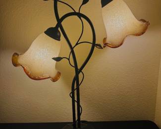 Elegant 2-Light Tiffany Style Table Lamp with Amber Art Glass Shades Description Beautiful decorative table lamp featuring two amber-frosted bell-shaped art glass shades with an elegant scrolling metal base and leaf accents. Gives off a warm, inviting glow and is perfect for a living room, bedroom, office, or entry table. * Two-light design * Frosted amber art glass shades * Decorative bronze/black metal finish * Fully tested and works perfectly * Excellent pre-owned condition A beautiful accent piece for traditional, Tuscan, Mediterranean, or transitional décor.