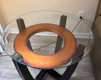 Add a sophisticated contemporary touch to your living room with this stunning three-piece occasional table set. The collection features a round tempered glass coffee table and two matching end tables, each showcasing a striking architectural base with black wood supports and a warm circular wood accent beneath the glass.