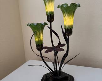 Art Nouveau Dragonfly Accent Lamp with Hand-Blown Art Glass Shades Description: Bring warmth and artistic elegance to your home with this beautiful three-light accent lamp featuring hand-blown green art glass tulip shades, graceful metal stems, and a decorative dragonfly centerpiece. The soft ambient lighting makes it a perfect statement piece for an entryway, side table, sunroom, or reading nook. Its nature-inspired Art Nouveau styling complements many Villages homes, especially coastal, cottage, traditional, and garden-inspired décor.