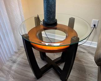 Add a sophisticated contemporary touch to your living room with this stunning three-piece occasional table set. The collection features a round tempered glass coffee table and two matching end tables, each showcasing a striking architectural base with black wood supports and a warm circular wood accent beneath the glass.