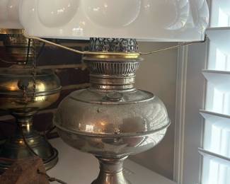 Silver Finish Hurricane Table Lamp — Decorative hurricane-style table lamp with a silvery metal base and a white milk-glass scalloped shade. The metal base shows an aged, distressed silver finish with surface wear and small spots of loss consistent with age; the shade is intact with no visible cracks. Works as an accent or bedside lamp and measures compactly for tabletops; clear wear gives it a softly aged, cottage or farmhouse look.