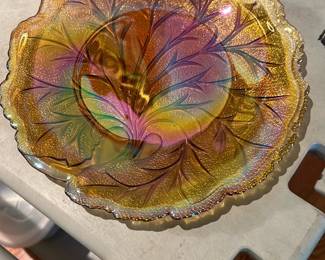 Carnival Glass Marigold Floral Bowl — Iridescent marigold carnival glass bowl with an embossed floral/leaf pattern and scalloped rim. The bowl shows vibrant orange-gold shimmer with purple and green iridescence depending on angle; textured center and detailed pressed design are visible in photos. Good solid condition with light surface wear consistent with normal use and no visible chips or cracks. A decorative accent piece well suited for display or as a small serving bowl; approximately medium-sized and fairly lightweight.