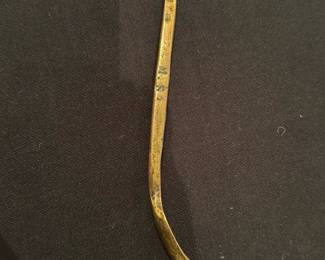 Brass Buttonhook — A slender brass buttonhook with a gently curved tip and flattened handle showing stamped initials "M.S.". The piece appears to be an older personal grooming or clothing accessory with surface wear, light verdigris and patina consistent with age. Solid, simple construction — useful for collectors of small brass tools or sewing notions; measures small and is lightweight. Condition is fair with visible wear and oxidation but no breaks.