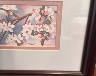 Framed Floral Print Cherry Blossoms — Framed floral print depicting a horizontal spray of cherry-blossom style flowers in pastel pinks and blues, matted with a double pink/gold inner mat and set in a dark brown molded frame. Clean glazing and matting appear intact with only normal surface reflections visible; frame shows light shelf wear at edges. A versatile decorative piece for bedroom or hallway display, lightweight and ready to hang or set on a tabletop.