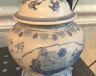Blue & White Ginger Jar — Decorative blue-and-white lidded ginger jar with floral motifs hand-painted in underglaze cobalt tones. Compact porcelain form with a domed lid and finial, scalloped neck border and petal band at the foot; shows light surface wear and a small glaze crazing visible on close inspection but no obvious chips or breaks. Good decorative condition and useful as a small storage jar or accent on a shelf or dining room cabinet. Measures as a small tabletop piece suitable for display.