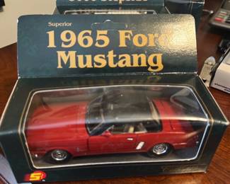 1965 Ford Mustang Diecast Model — This boxed 1965 Ford Mustang diecast model is a collectible replica in red with a black roof, presented in its original display packaging. The model shows detailed exterior trim, chrome wheels, and clear display window on the box, making it ideal for collectors or office display. Packaged size is small and tabletop-ready; sold as-is from the office room and appears unopened though box shows light shelf wear. Overall condition is good with some scuffs to the outer box but the model appears intact inside.