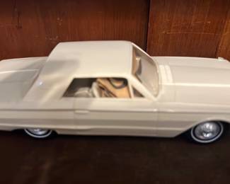 White 1964 Ford Galaxie Model Car — Diecast model of a white 1964 Ford Galaxie (hardtop coupe styling) shown from multiple angles with detailed undercarriage stamping and hubcap-style wheels. The model features a cream/white exterior, tan interior, and realistic molded chassis text visible on the underside. Good overall display condition with light surface wear and no visible major breaks; paint and trim appear intact. A solid piece for collectors of classic American car models or as a display accent in an office or den.