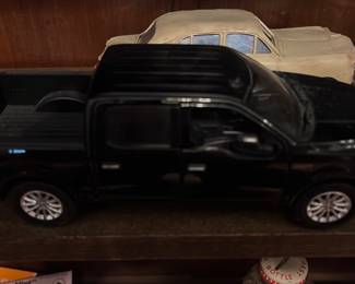 Black Pickup Truck Toy — Black pickup truck diecast model with crew cab and detailed undercarriage. Molded plastic and metal construction with silver-painted alloy-style wheels and spare tire under the bed; good tabletop/display piece with light surface scuffs consistent with handling. No visible brand or scale markings on exterior (see underside detail in photos). Measures compactly and is suitable for shelf display or as a collectible toy truck.