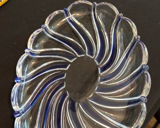 Mikasa Glass Swirl Serving Platter — Mikasa clear glass serving platter with molded swirl ribs and applied cobalt-blue accents along the ridges. The platter is from Mikasa (box shown) and displays a decorative, slightly scalloped oval profile suitable for serving or display. Photos show the piece in intact condition with no obvious chips or cracks; surface shows light use and shelf wear consistent with prior use. Approximately medium size — good for dining-room or buffet service.