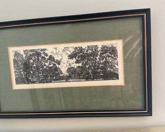 Framed Black & White Tree Print — Framed black-and-white panoramic print showing a row of large trees and small buildings, double-matted with a green linen mat and simple black frame with gold trim. The piece is decorative and ready to hang; glazing appears intact but has surface reflections in photos. Good condition with light age toning to the paper visible at the inner mat edge and only minor scuffs to the frame edges.