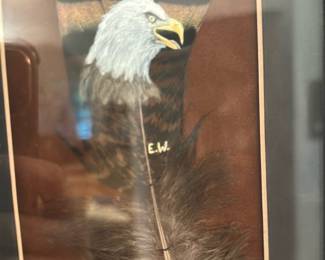 E.W. Eagle Feather Framed Art — Framed mixed-media feather artwork signed with visible initials "E.W." depicting a painted bald eagle head on a mounted feather. The piece is double-matted in earth tones and set in a dark wooden frame with glass; subject and signature are clearly visible. Good condition overall with light surface/age wear to mat and frame and intact glass; feather display appears secure. Compact wall artwork that suits a study or living room.