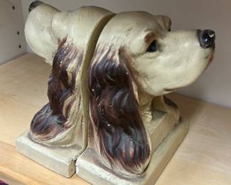 Spaniel Dog Bookends — A pair of spaniel head bookends cast in a painted plaster or composite material, shown as a matching left and right set. The sculpted long ears and painted brown-and-cream finish give these decorative bookends a cottage- or country-style charm; they sit on rectangular bases and show surface wear and small paint rubs consistent with age and use. Solid, decorative pieces ideal for bookshelf display; see photos for condition and wear.