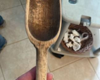 Hand-Carved Wooden Scoop — Hand-carved wooden scoop with a long handle and deep oval bowl, shown with natural age wear and a warm patina from use. Solid, likely hardwood construction with surface abrasions and darkening inside the bowl consistent with years of service; no visible cracks or breaks. Useful as a rustic kitchen scoop, pantry measure, or decorative accent for farmhouse or cottage-style displays. Measures approximately as noted and sold as a single piece in its shown condition.