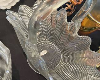 Pressed Glass Leaf-Pattern Basket — Clear pressed-glass handled basket with a radiating leaf/rib pattern and molded beaded center. The heavy molded handle attaches to a flared petal-like bowl with scalloped edges; piece displays typical mold seams and light surface wear consistent with use. Good decorative condition with no obvious large chips or cracks visible in photos; great as a table centerpiece or for seasonal display. Measures medium size and pairs well with other vintage glassware on a serving or display table.