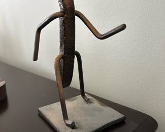 Vintage Welded Nail Art — Handcrafted welded sculpture made from a bent iron nail and welded rod limbs mounted on a square iron base. The minimalist figure stands in a walking pose with textured head and patinated dark metal finish; signs of surface oxidation and light wear are visible on the base and feet. A small decorative object that works well on a shelf or desk; solidly welded and stable on its metal base. Measures compactly and is simple to display as an industrial-style accent piece.