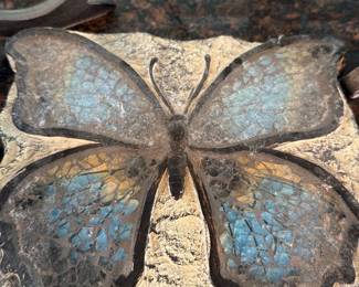 Garden Stone — Garden Stone is a decorative cast-stone butterfly garden plaque with textured, weathered finish and mottled blue and tan painted wings. Shown resting on a counter, the piece appears to be a solid, heavy garden ornament suitable for a planter edge or yard accent; finish shows expected surface wear and patina consistent with outdoor use. No maker's mark or dimensions are visible in photos; condition is fair with worn paint and surface dust as pictured. Lightweight enough to move by hand but substantial for outdoor display.