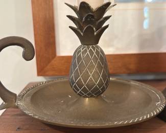 Brass Pineapple Chamberstick — Brass chamberstick with a decorative pineapple-form candle cup and rope-edge tray; the small handled candlestick is solid metal with an aged patina and light surface wear consistent with use. The pineapple motif and compact size make it a charming accent for mantels or bedside tables; it holds a standard taper as shown. Good structural condition with some surface spotting and minor scratches visible in photos. Measures small and easy to display as a single decorative candleholder.
