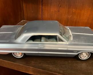 1964 Chevrolet Impala Model Car — Diecast model of a 1964 Chevrolet Impala in metallic light blue with detailed undercarriage molding and period-style hubcaps. The model shows intact wheels and a clean paint surface with light shelf wear consistent with display use; no visible broken parts. A good display piece for collectors of classic American cars or as a shelf accent in an office. Measures roughly the length of a standard model car and appears complete from the photos.