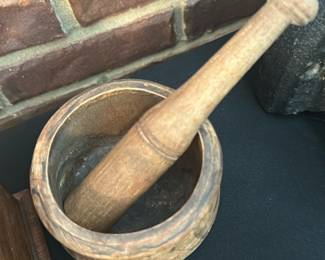 Wooden Mortar and Pestle — Hand-carved wooden mortar and matching pestle with a rustic patina and visible wear consistent with age and use. The round mortar has a carved exterior band and the pestle shows smoothing from handling; both pieces are solid and sturdy for display or light kitchen use. No maker's marks or labels visible; condition is good with surface wear and small dents from use. Compact size makes it suitable as a decorative kitchen accessory or for light grinding tasks.