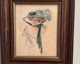 Framed Woman in Hat Portrait — Framed pencil and watercolor portrait of a woman wearing a wide-brim hat with a long dark ribbon and blue feathering. The image is on a light fabric or paper substrate and is set in a carved wood frame with an inner gilt liner; subject and loose sketching suggest early 20th-century fashion illustration style. Overall condition is good with light age toning to the support and minimal surface wear to the frame visible in photos. Frame outer dimensions approximate a small wall piece suitable for bedroom or hallway display.