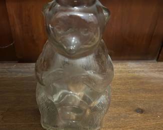 Snow Crest Bank Bottle — Clear glass bear-shaped bottle with a metal screw-on lid stamped "SNOW CREST BANK BOTTLE" in red; the lid has a coin slot making this a novelty bank bottle. Molded glass shows textured fur detail and intact form with minor surface wear and light scuffs consistent with age. Great display piece for collectors of milk-bottle-era novelties or advertising memorabilia; measures small and is easy to shelf. Lid shows paint wear around the edge but remains functional as a coin bank.