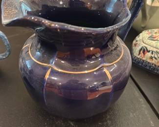 Cobalt Blue Ceramic Pitcher — Handsome cobalt blue glazed ceramic pitcher with a scalloped rim, molded handle and subtle gold-painted banding and accents. The piece has a rounded bulbous body and appears to be handmade or studio-produced with a rich deep glaze and speckled inner rim detail. No maker's marks or printed brand are visible on the base in photos; condition is good with light surface wear and glaze irregularities consistent with age and use but no obvious chips or cracks. Compact size makes it suitable as a decorative vase or serving pitcher.