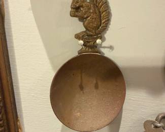 Cast Iron Squirrel Wall Hook Spoon — Decorative cast-iron wall hook shaped with a squirrel finial and a shallow scoop/holder below. Heavy, rustic metal with a worn brown/gold finish and surface rust in the bowl; two mounting holes visible behind the squirrel. A small, quirky piece that works as a key or coin holder, herb scoop, or accent hook; solid cast construction but shows age-related surface oxidation and wear consistent with vintage use. Measures compactly and mounts with two screws as shown.