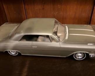 Gray Classic Car Model — Metal diecast classic car model in silver-gray with detailed molded underside and chrome-look hubcaps. Solid cast body with painted finish, interior seats visible through windows, and realistic chassis detail on the bottom. Appears structurally sound with light surface wear consistent with display use; no box or paperwork shown. Compact collectible suitable for display on a shelf or in a model car collection.