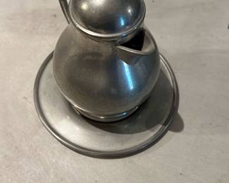 Pewter Creamer with Underplate — Small pewter creamer with matching underplate shown in photos. Rounded bulbous form with hinged lid, short pouring spout and loop handle; the underplate is plain with a raised inner rim. Piece shows light surface wear and fine scratches consistent with age and use but no visible dents or repairs. A compact table accessory for collectors of pewter or vintage tableware; measures approximately as listed below.