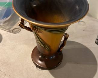 Roseville 906-6 Vase — Roseville pottery vase marked "Roseville 906-6" on the base, a classic mid-century American art pottery piece with a warm mottled brown-to-amber glaze and applied rope-style handles. The vase stands with a flared trumpet mouth and round foot, showing even glaze depth and gentle surface wear consistent with age but no obvious chips or large cracks in photos. Roseville produced many popular art pottery lines in the early-to-mid 20th century; this piece would suit collectors of American art pottery or as decorative display. Sold as-is; buyers should inspect for hairlines or restoration not visible in photos.