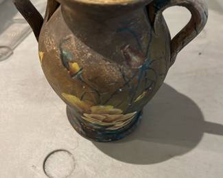 Hand-Painted Two-Handled Vase — Decorative two-handled earthenware vase with hand-painted floral motif in warm ochre and green tones. The piece has a dark glazed interior and a matte exterior with painted yellow flowers and vine detailing; brushwork appears amateur-to-studio made. Shows surface wear and light scuffs consistent with age and use but no obvious cracks visible in the photos. Compact accent vase suitable for shelf display or as a decorative collector's piece; measurements are estimated below.