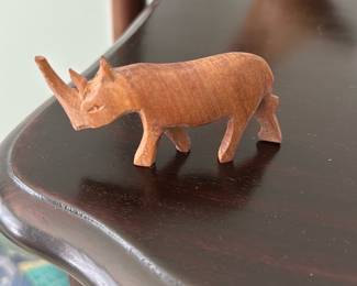 Hand Carved Wooden Rhino Figurine — Small hand-carved wooden rhinoceros figurine with a smooth, warm finish and simple, folk-style carving. Solid wood construction with carved horn and stylized legs; no visible maker's marks. Good condition with minor surface wear consistent with age and handling. Perfect as a shelf accent or part of a carved-animal collection; compact size shown in photos.