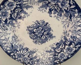 Bonn Wildrose Blue Transfer Plate — Decorative blue-and-white transferware plate marked "Bonn Wildrose Germany" featuring an ornate floral center and dense floral border. The plate is ceramic/porcelain with visible crazing consistent with age and displays a maker's mark on the back reading "Bonn Wildrose Germany" with a crest and date marking. Plate is ideal for wall display in the living room; useful as decorative dinnerware but sold primarily as a collectible display piece. Condition is good for age with surface crazing and light wear but no visible large chips or cracks in photos.