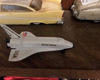 USA Space Shuttle Toy — Small plastic USA space shuttle toy with white upper fuselage, black nose and underside, and printed American flag on the tail. Lightweight shelf/display model with simple molded landing gear and minor surface wear consistent with play or age; no box or markings indicating manufacturer are legible in the photos. Measures compactly and is suitable for a desk or small collection of die-cast and plastic vehicles.