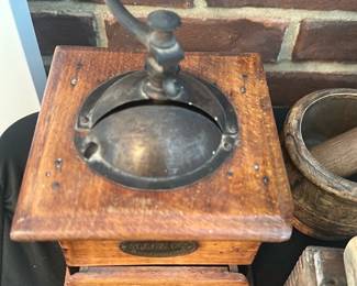 Cast Iron Coffee Grinder — Small antique cast-iron and oak coffee grinder with crank handle and pull-out grounds drawer. Solid wooden base and metal top show age-appropriate wear, surface rust on the iron and light scuffs to the wood; hardware intact and drawer functional. Decorative brass maker plate visible but text worn; a great piece for collectors or rustic kitchen display. Measures small tabletop size and is shown with other rustic items.
