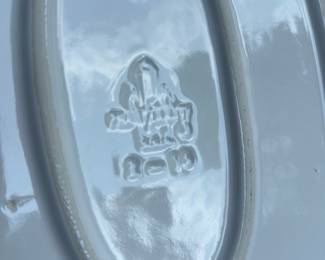 White Ceramic Oval Serving Platter — White glazed ceramic oval serving platter with a raised inner well and molded rim detail; maker's mark impressed on the base (photographed) but not fully legible. Appears to be a medium-sized serving piece suitable for sides or small roasts, with light surface wear consistent with normal use and no obvious chips or cracks visible in photos. Neutral white glaze fits a variety of table settings and is stackable with similar platters. Sold as shown; buyer should inspect maker's mark if maker attribution is required.