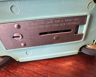 Turquoise Tin Coin Bank Car — Mid-century style turquoise metal toy car that doubles as a coin bank with slot and winding key access on the underside. Made of painted metal with plastic windshield and rubber-tread wheels; features interior bench seating and chrome-look bumpers. Approximately 12 inches long and light enough for display on a shelf or desk; great as decor or collectible. Good overall condition with surface wear to paint, light scratches, and some patina on metal parts; bank mechanism appears intact though not tested.